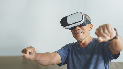 Happy Asian Senior Adult is using VR glasses headset with virtual reality motorcycle game at home.