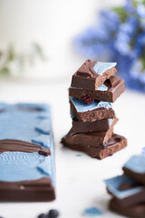Bites of blueberry dark chocolate bar on a marble table with lilac and berries on it. Craft chocolate bars closeup.   