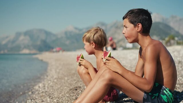Happy kids eating big red slices of watermelon on the beach.