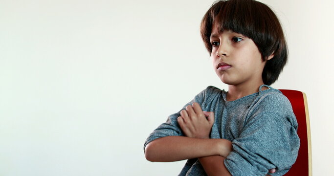Pensive child boy sitting on chair thinking, kid crossing arms feeling upset emotion