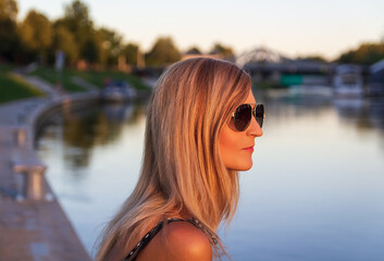 Portrait young blonde woman with sunglasses and ships in port, river Vltava, city Ceske Budejovice at sunset