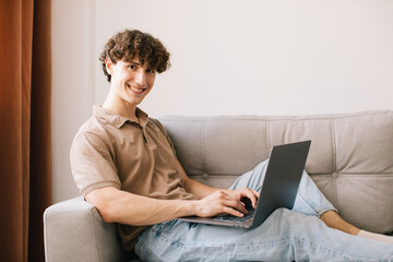 Portrait of attractive young curly hair man using laptop while sitting on sofa at home