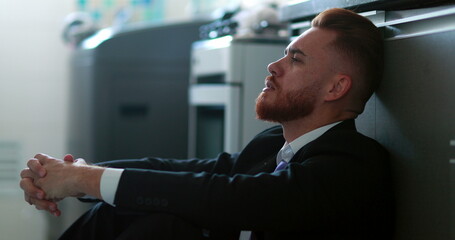 Man wearing business suit sitting on home floor feeling despair and anxiety for the future