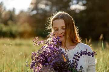 Close up portrait of young beautiful redhead woman with freckles, wearing white dress, posing in the nature. Girl with red hair holding flowers. Natural beauty. Diversity, individual uniqueness.