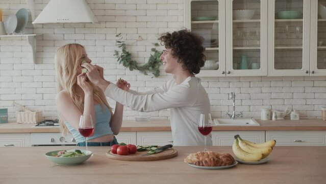 Young beautiful couple in plaid shirts are cooking at home in the kitchen. A woman and a man cut vegetables and make a salad of pepper, tomato, cucumbers, radish in a transparent glass dish.