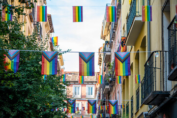 Streets of the Madrid neighborhood of Chueca adorned with rainbow flags on the occasion of LGBTI and gay pride week, during a sunny summer day - obrazy, fototapety, plakaty