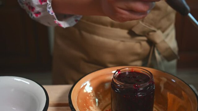 Close-up of a pastry chef filling a sterile glass jar of freshly brewed fruit jam