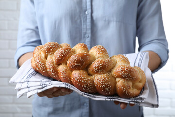 Closeup view of woman holding homemade braided bread near white brick wall. Traditional Shabbat...