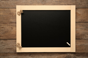 Clean small blackboard with piece of white chalk on wooden table, top view