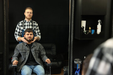 Fototapeta na wymiar Professional hairdresser working with bearded client in barbershop