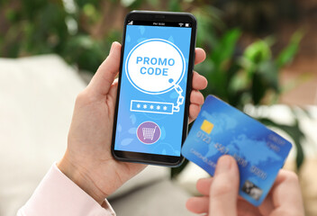 Woman holding credit card and smartphone with activated promo code in online shopping app indoors,...