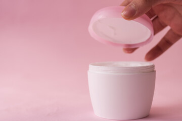 Hand opening a skin cream bottle for women on pink background