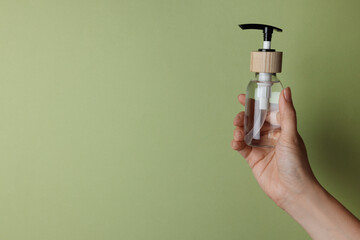 Woman holding bottle of cosmetic product on pale olive background, closeup. Space for text