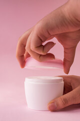 Hands opening a skin cream bottle for women on pink background