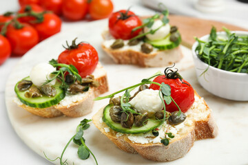 Tasty bruschettas with capers, vegetables and mozzarella served on white marble board, closeup