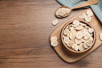Obraz na płótnie Canvas Bowl and spoon with dried banana slices on wooden table, flat lay. Space for text
