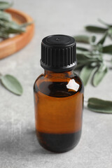 Bottle of essential sage oil and leaves on light grey table