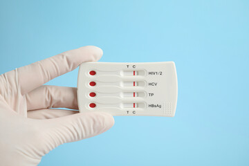 Fototapeta na wymiar Doctor holding disposable express test for hepatitis on light blue background, closeup