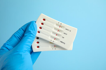 Doctor holding two disposable express tests for hepatitis on light blue background, closeup