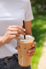 Woman holding takeaway plastic cup with cold coffee drink outdoors, closeup