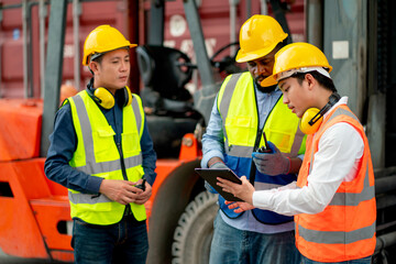 African American cargo container worker discuss with Asian technician using tablet in workplace area and they stay near forklift car.