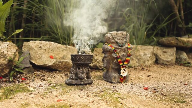 Incense burner with incense burning and native statue in tropical garden in Tulum on a sunny afternoon 