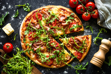 Pizza on black background. Traditional italian pizza with prosciutto, cheese, tomatoes and arugula...