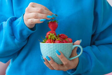 One hand holds a yellow bowl with strawberries the other holds one berry by the stem