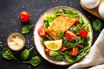 Green salad with salmon fillet. Healthy lunch, diet nutrition. Top view on black.