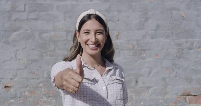 Female expressing satisfaction and positivity with a like thumb emoji finger in town. Girl giving a finger sign in thanks downtown. Portrait of happy woman showing a thumbs standing in the city alone