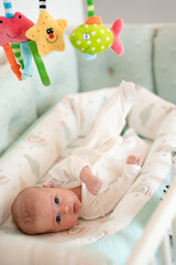 A newborn baby is lying in his crib and looking at toys suspended from above