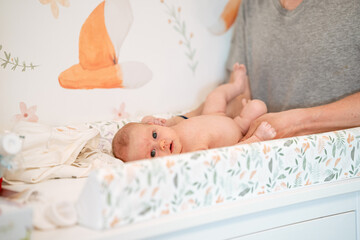 A father changes a diaper for a newborn baby on a changing table - obrazy, fototapety, plakaty