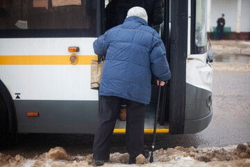 Pensioner enters bus. Old woman in Russia. Grandmother with stick for support when walking. Human...