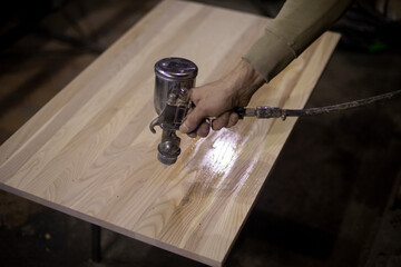 Applying varnish to board. Spray gun for paint supply. Instrument is in hand of man. Wood...