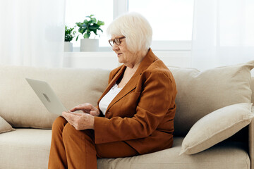 an elderly businesswoman is sitting on a beige sofa in her bright apartment and carefully looks at...