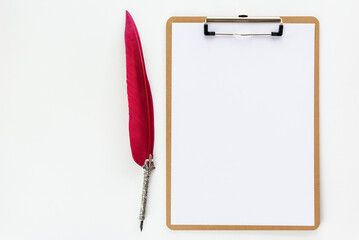 Top or above view / flat lay of office supply on designer desk table, business / personal work space, blank sheet a4 paper on clipboard, quill feather pen, empty space for text / schedule. White theme