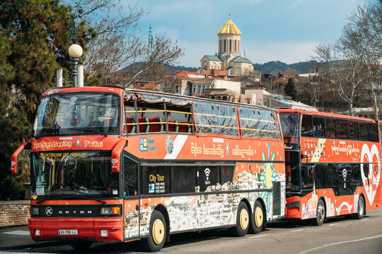 Tbilisi, Georgia - March 28, 2022: View On Red Hop On Hop Off Tourist Buses Setra S228dt In A City Street. Famous Landmark Metekhi Church On Background. Big Buses On Old Street In Tbilisi. big Bus
