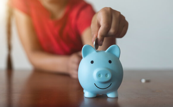 Smiling little girl posing with a piggy bank in her hands, standing against a blue background in a studio with free space. Family savings