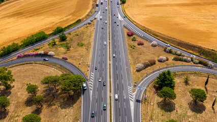 Motorway interchange in Italy. Each carriageway with three lanes of travel. On the sides of the road there are fields of wheat. There are no cars on the asphalt.
