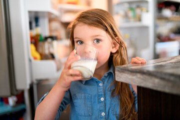 beautiful girl drinks milk on the glass in the kitchen
