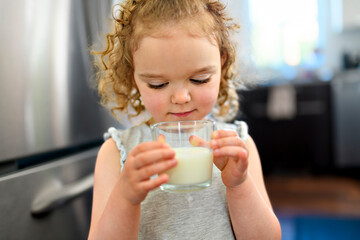beautiful girl drinks milk on the glass in the kitchen