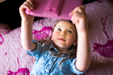 little girl playing tablet lay on the bedroom