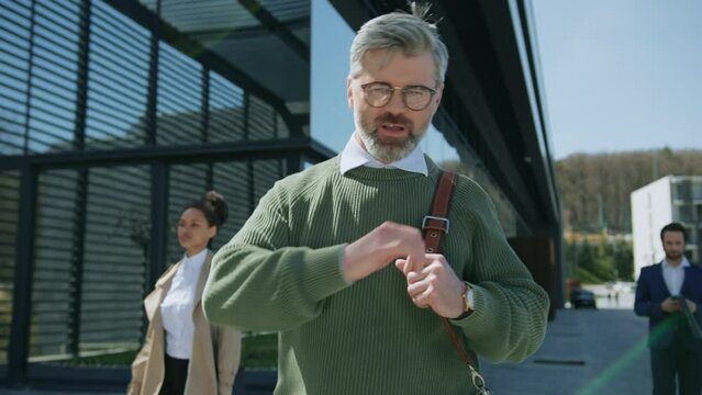 Attractive happy man with beard and glasses actively dancing while walking down the street near business center. People around. Businessman. Sunlight. Slow motion