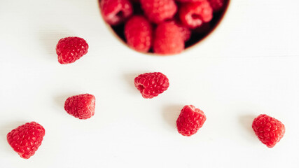Fresh red raspberries in a paper cup on a white table background