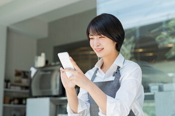 Obraz premium カフェ スマートフォンを使う女性スタッフ
