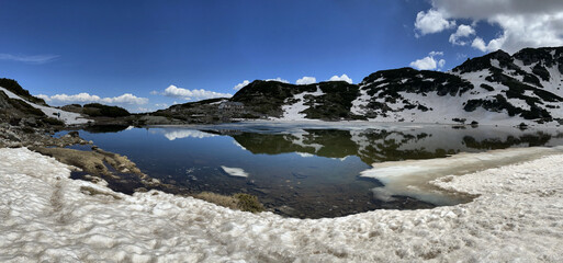 Berge mit letztem Schnee im Frühling spiegeln sich im Wasser von einem der sieben Rila Seen im...
