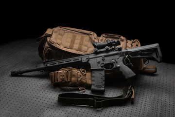 A modern automatic carbine with a collimator sight. The weapon lies on a military backpack. Rifle for the police, special forces or the army. Dark back. - obrazy, fototapety, plakaty