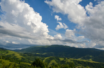 Summer landscape of mountain ridge covered with lush grass and dense forest on cloudy day. Carpathian Mountains, Ukraine