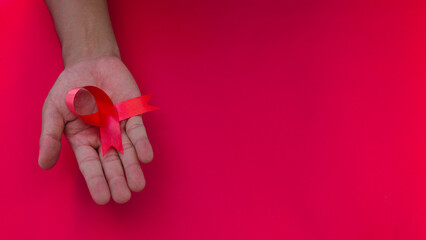 Hand holding a Red AIDS Ribbon with copy space for text isolated on red background