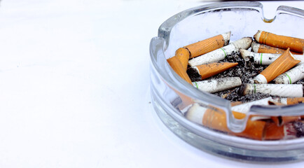 Lots of dirty used cigarette butts in an ashtray on a white background. Glass ashtray. Health, smoking, unhealth, Lung cancer. View from above. Copy text space